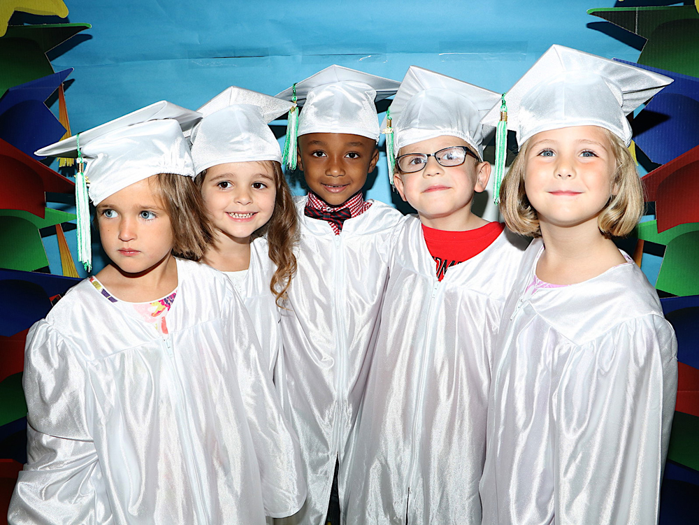  5 children stand next to each other in cap and gown ready to graduate 