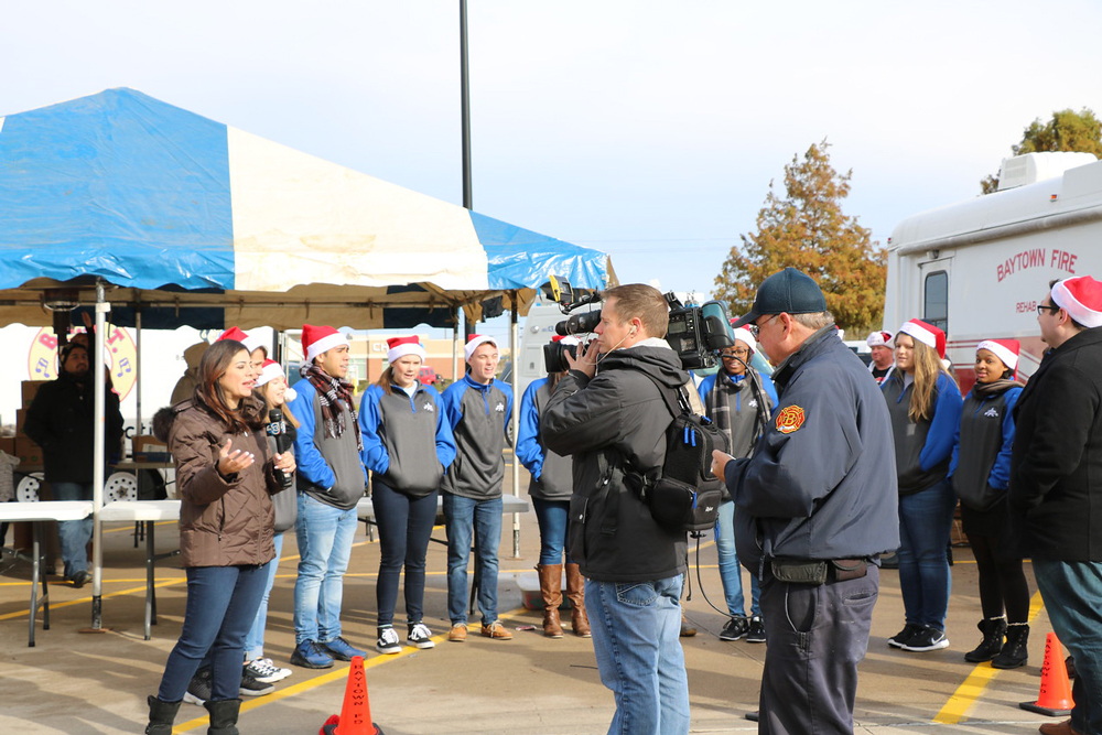 
Patricia Lopez from Channel 13 is live from the Walmart (Garth Road) parking lot with the Ross S. Sterling High School Swing Choir for the annual Share Your Holidays Food Drive. Also pictured are Channel 13 cameraman Charles Fisher (front middle), Jimmy Moss with the Baytown Fire Department and Levi Duncan (right), RSS choir director. This is the 37th year the Baytown/Highlands community has participated in the food drive.
