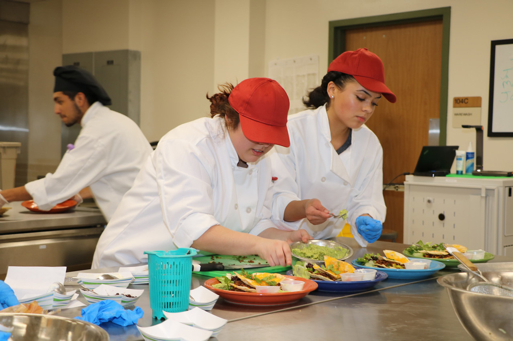  From left, Mildreth Sandate and Naomi Carney from Robert E. Lee High School put the finishing touches on their Latin-inspired pizza and Latin salad with fresh guacamole during the recent Latin Fusion – Lone Star Chef Competition, while Brayan Franco (back) from Ross S. Sterling High School helps complete his team’s entry.