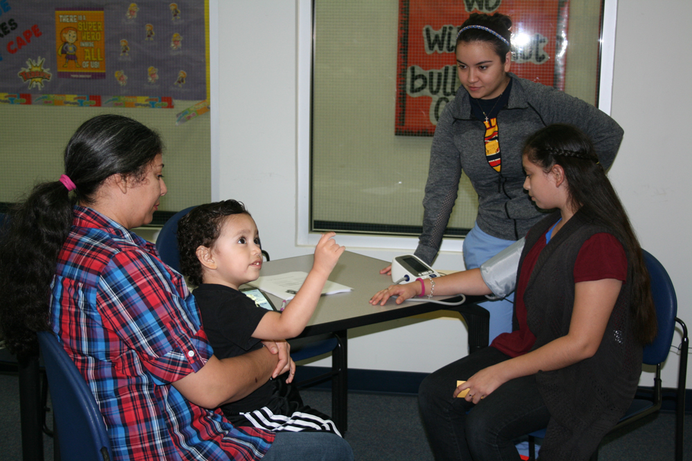 Rosa Melendez (right), Carver nurse, checks Carver student Paula Guajardo and her mother’s blood pressure at Carver CATCH Family Night.