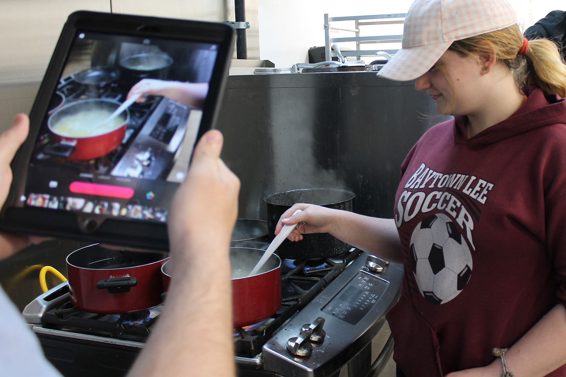 Student tries new recipe while other student videos on ipad.