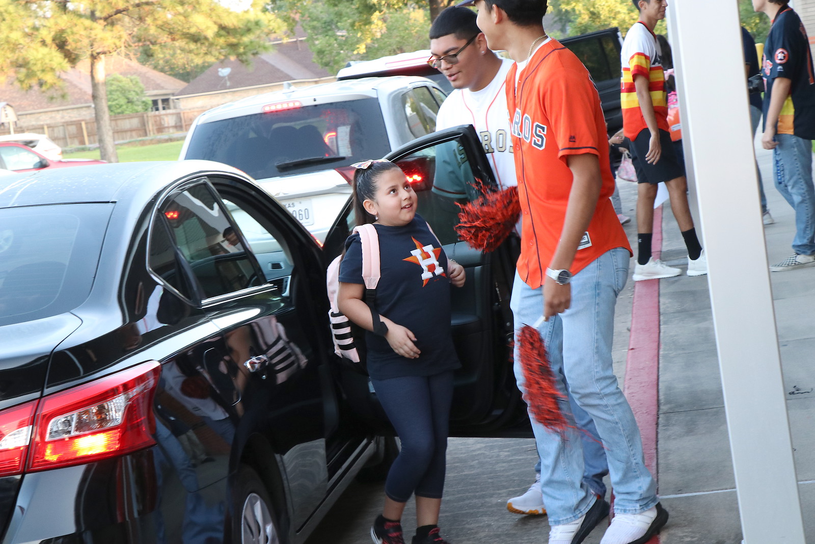 Robert E. Lee High School baseball players (left) Sergio Cortes and Izayah Hernandez help Travis Elementary third-grader Julacy Torres with the car door as she arrives at school.