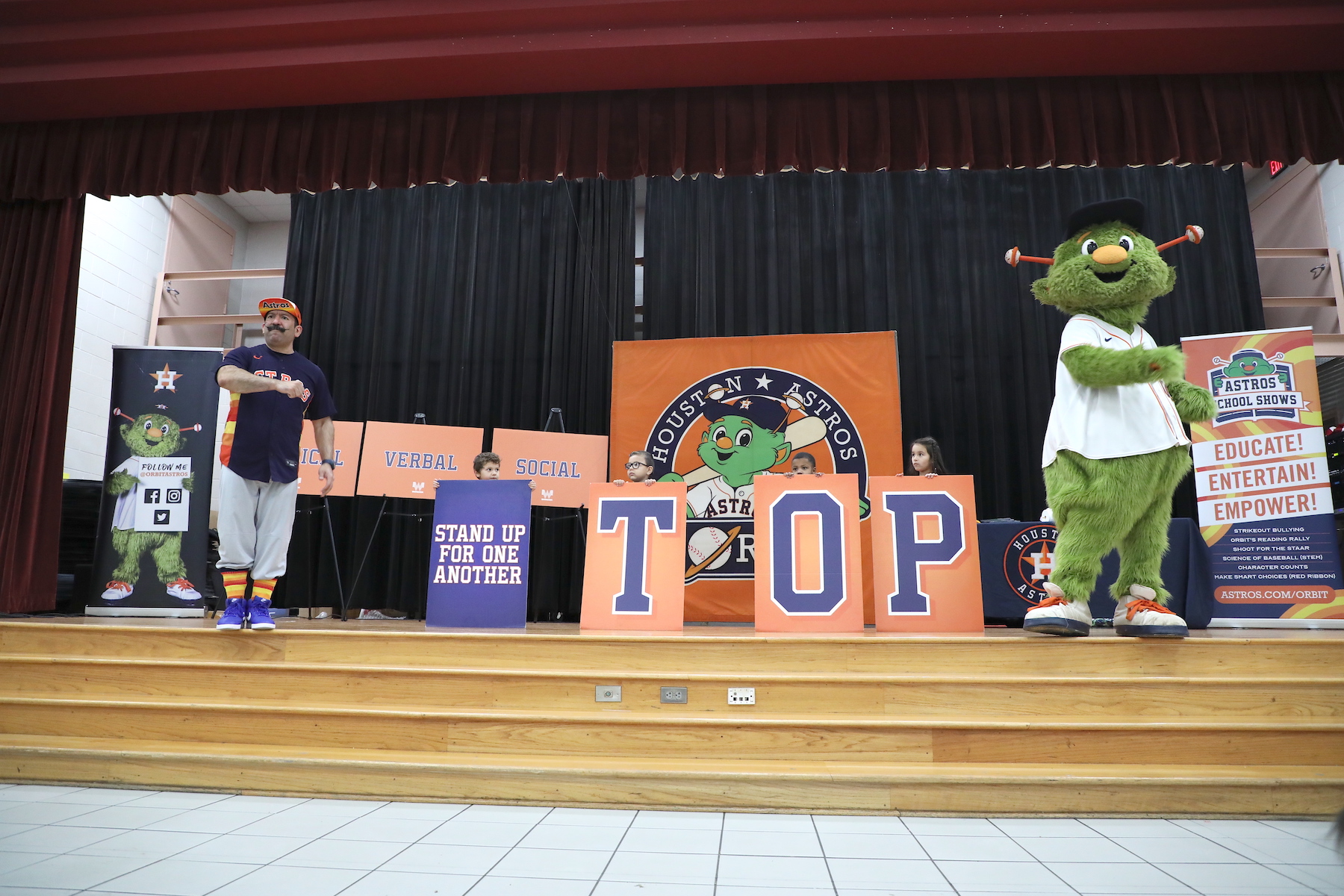orbit and astros representative speak on stage while students stand behind signs that spell out stop