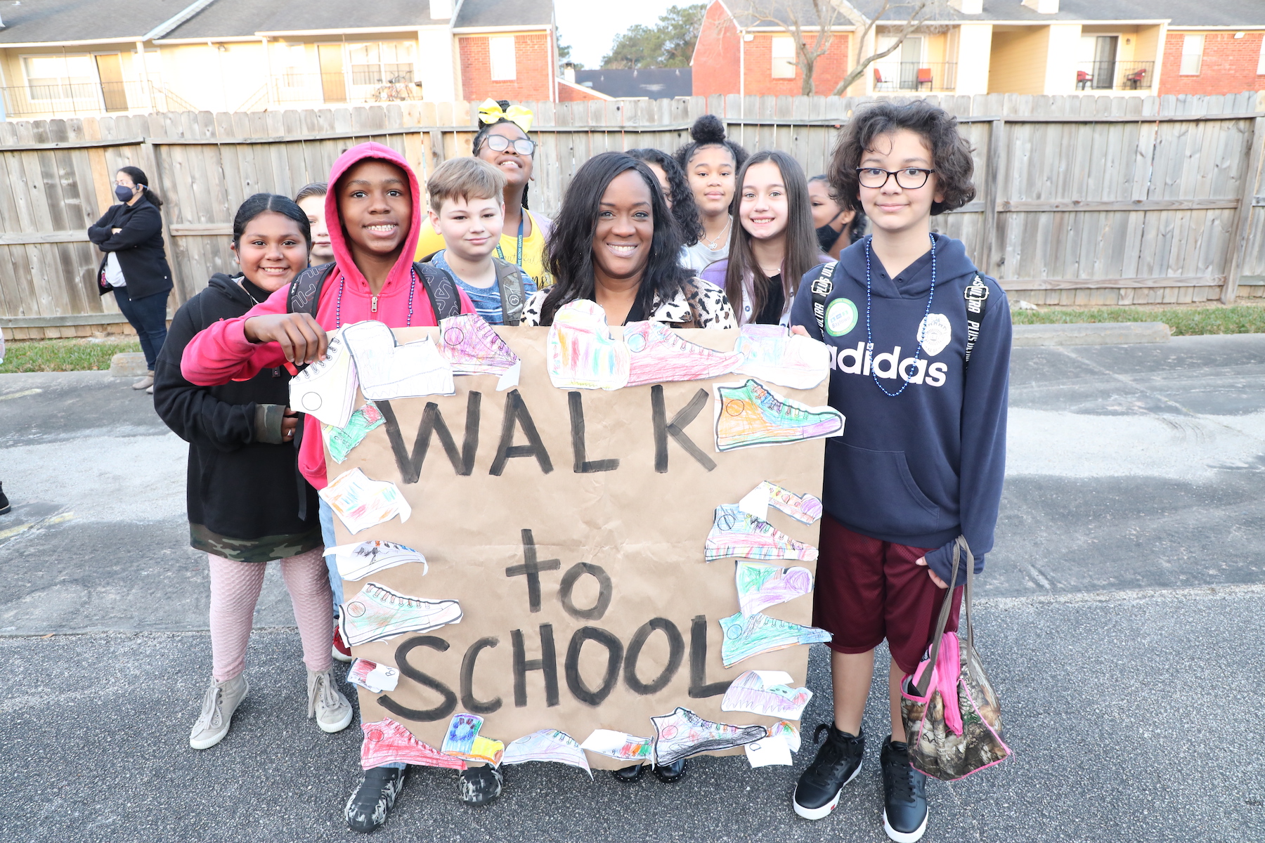 students pose outside with teacher holding a walk to school sign before walking to school