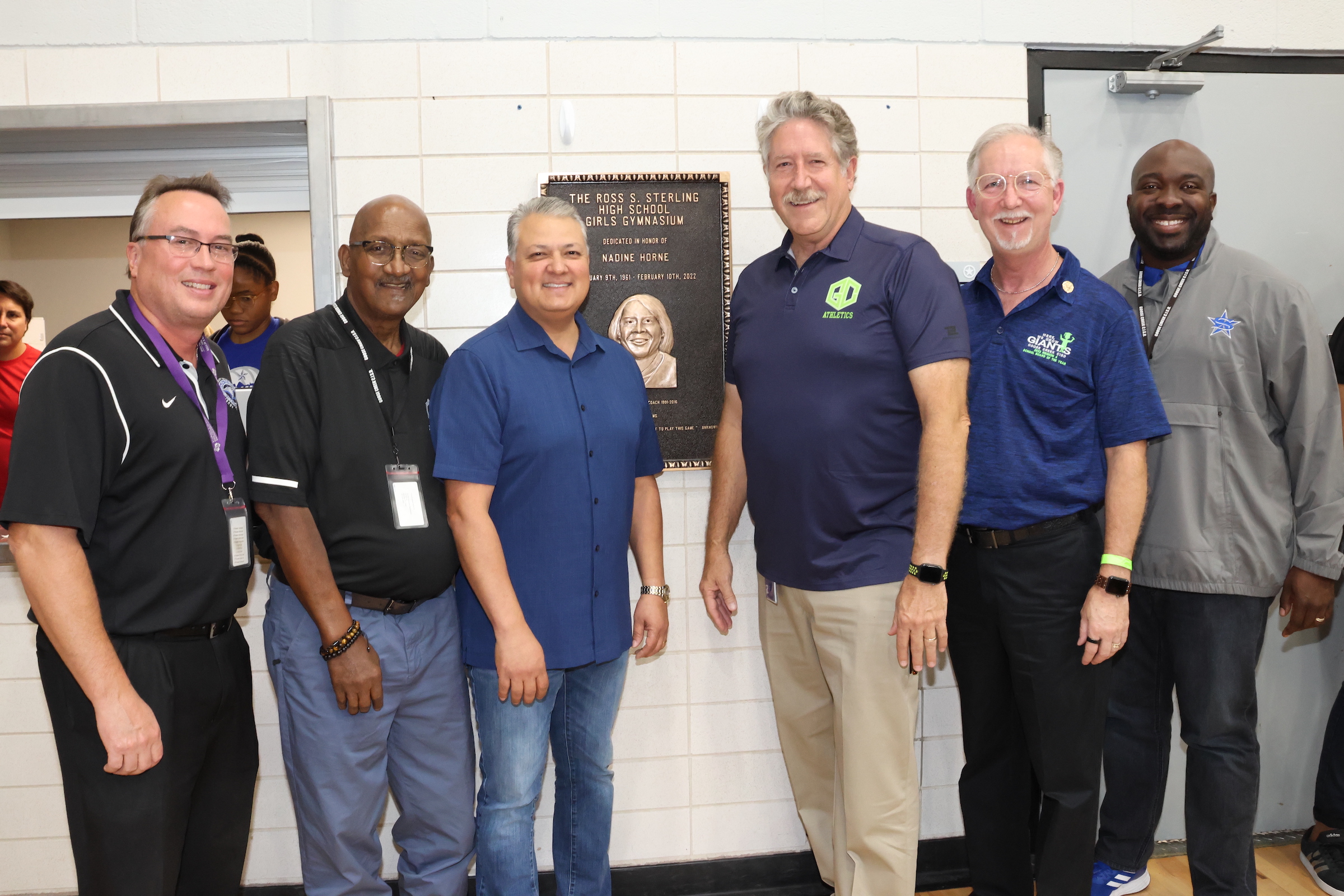 District admin and board members pose with nadine horne plaque in sterling gym