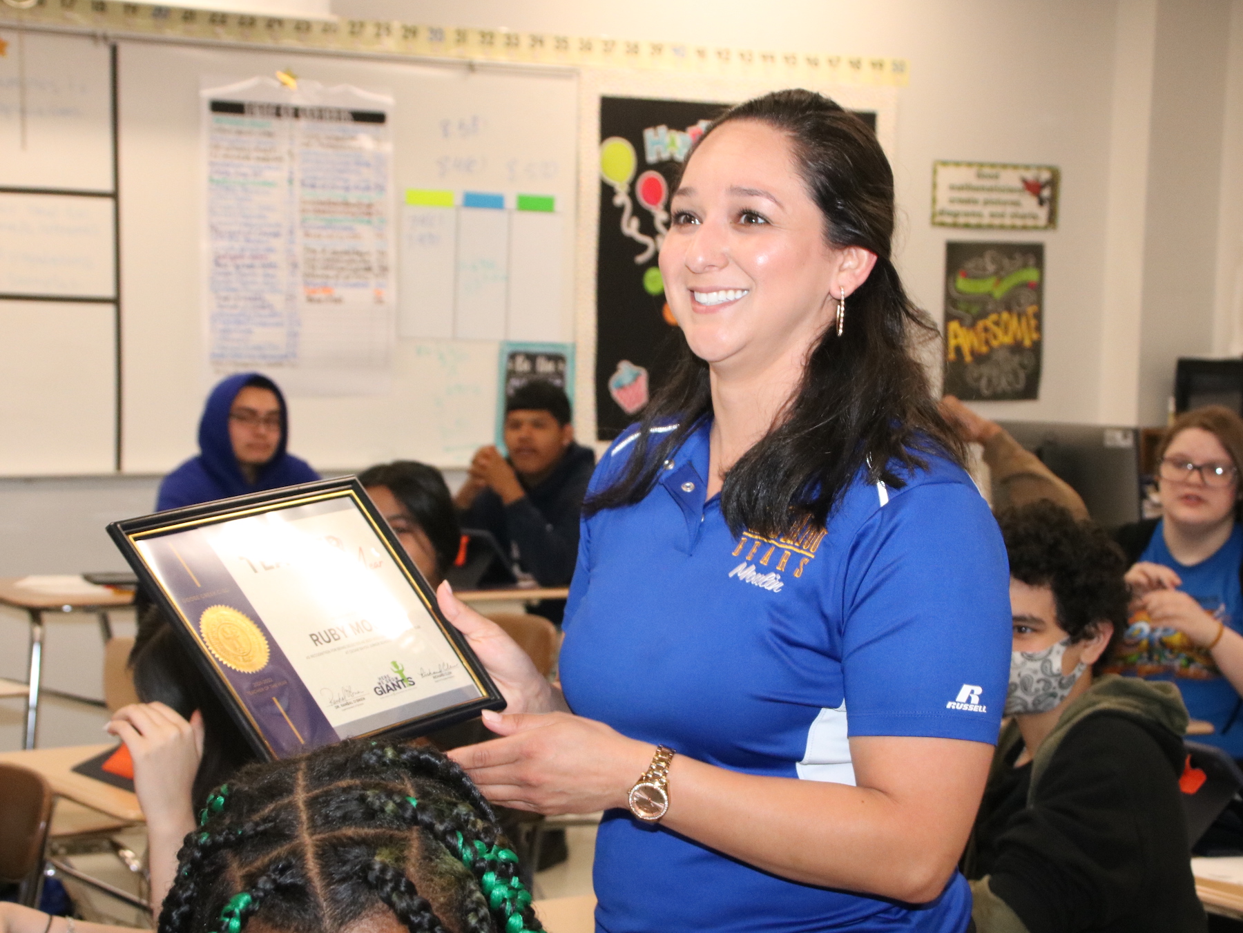 Teacher in classroom smiling with excitement while holding plaque