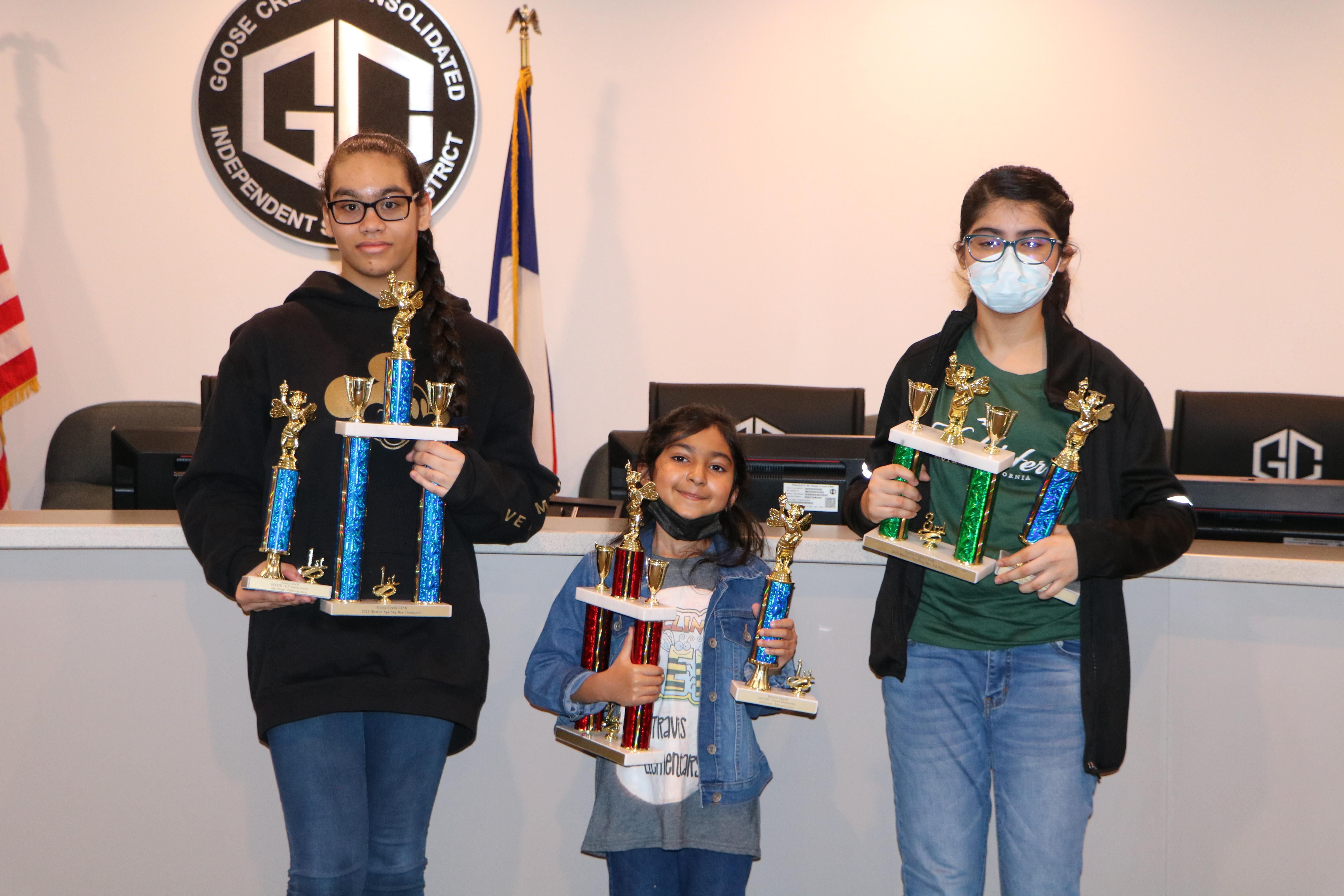 Top three winners pose in the board room with their spelling bee trophies.