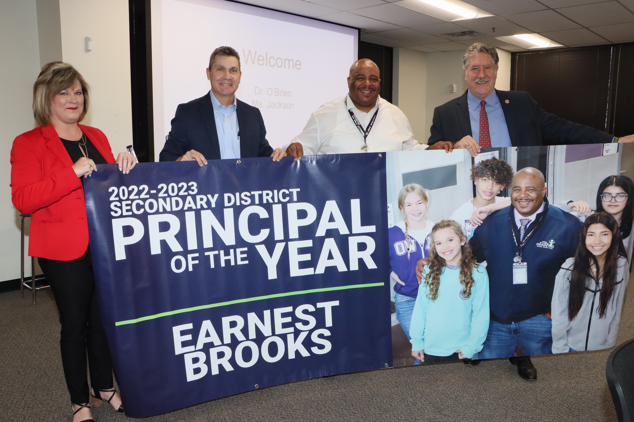 Earnest Brooks holds principal of the year banner with district administrators
