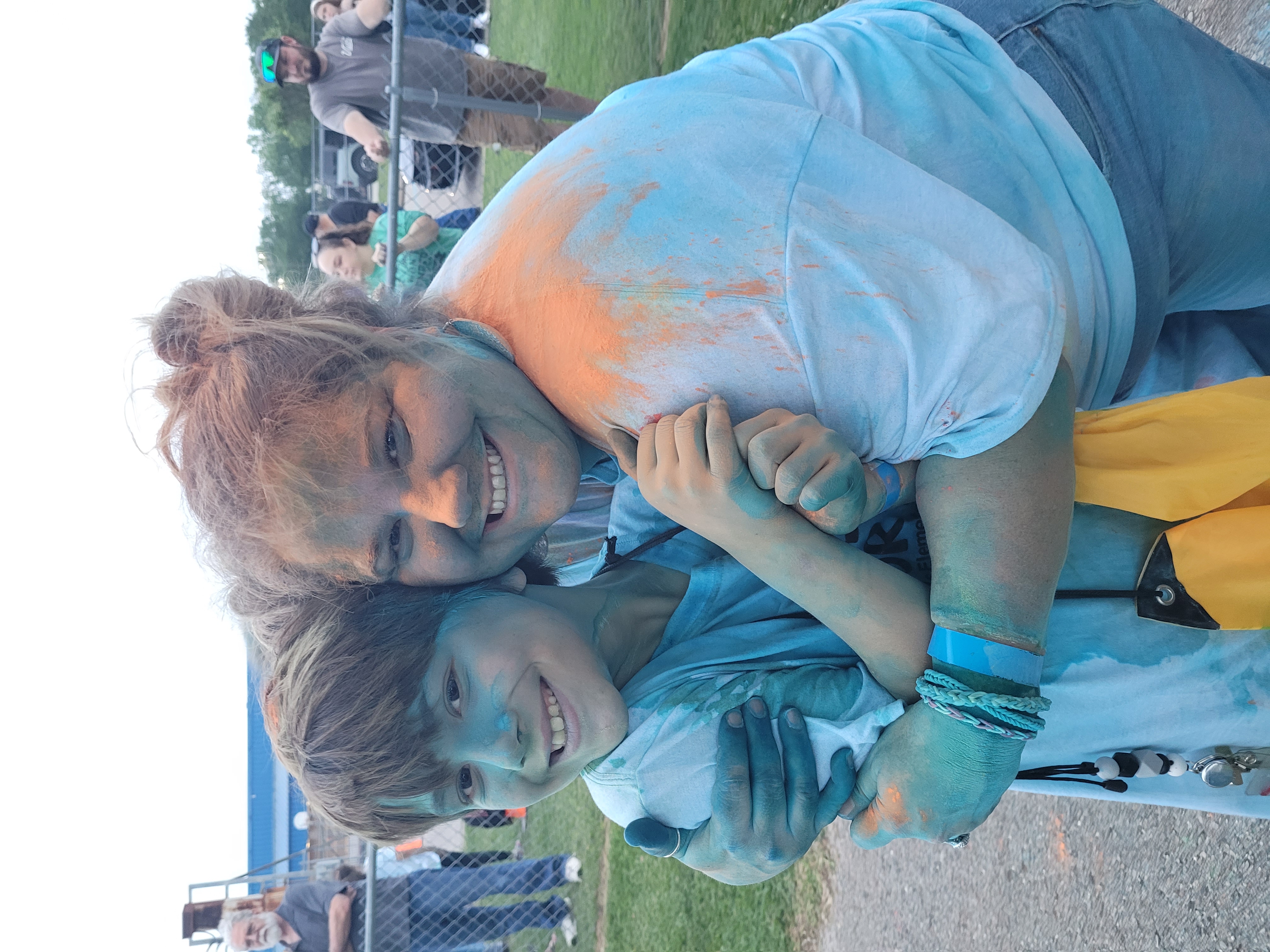 staff members hugs student covered in color powder