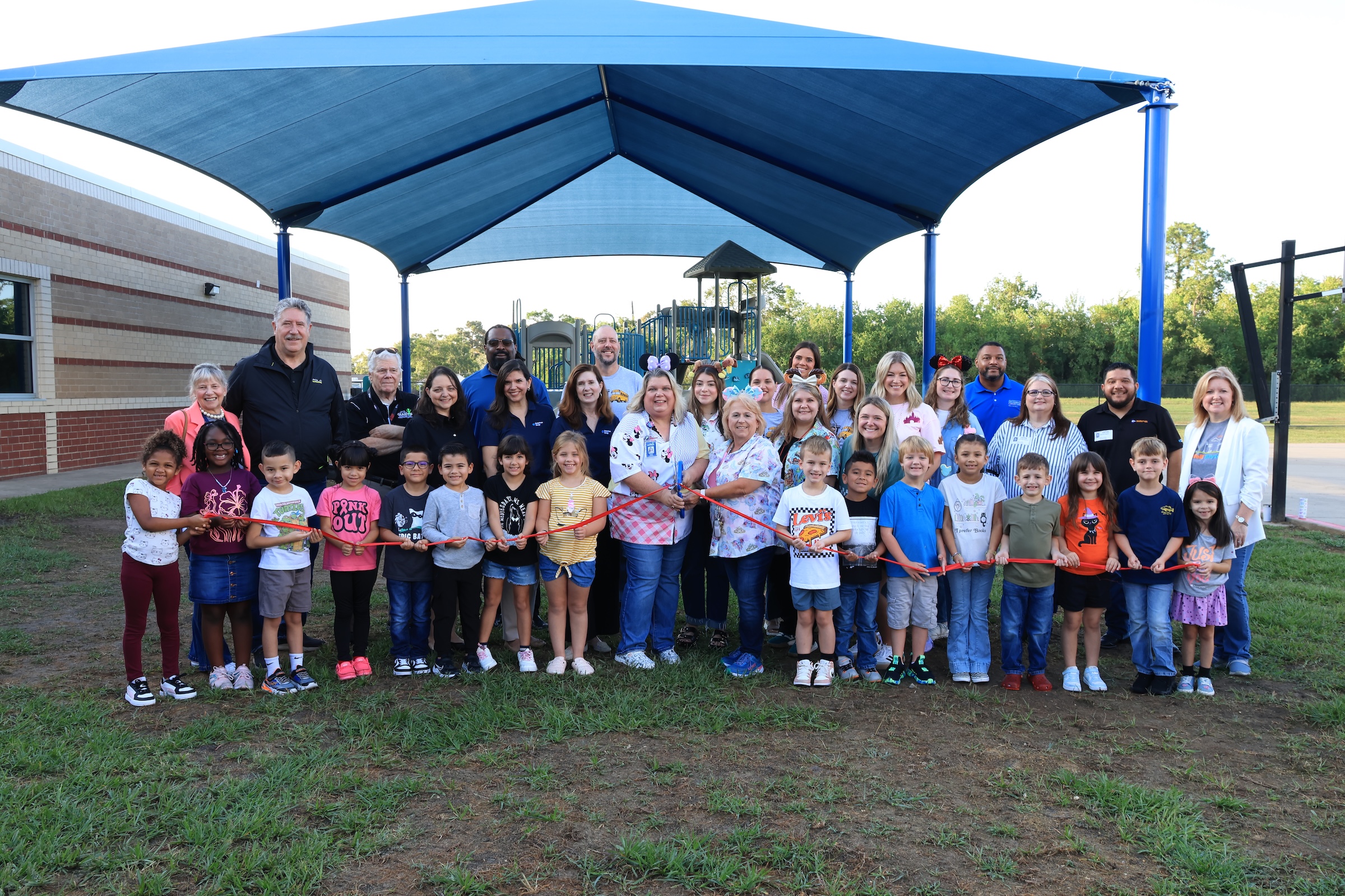 district leaders, community representatives, and students hold a red ribbon to cut