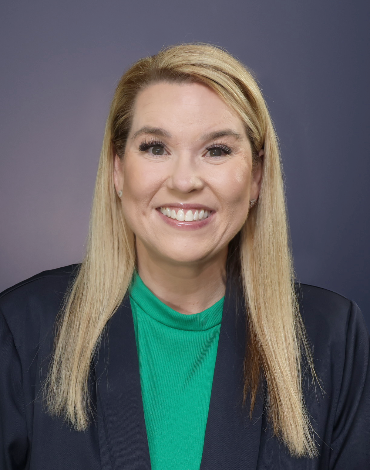 Marissa Phillips smiling while wearing a navy blazer and green shirt