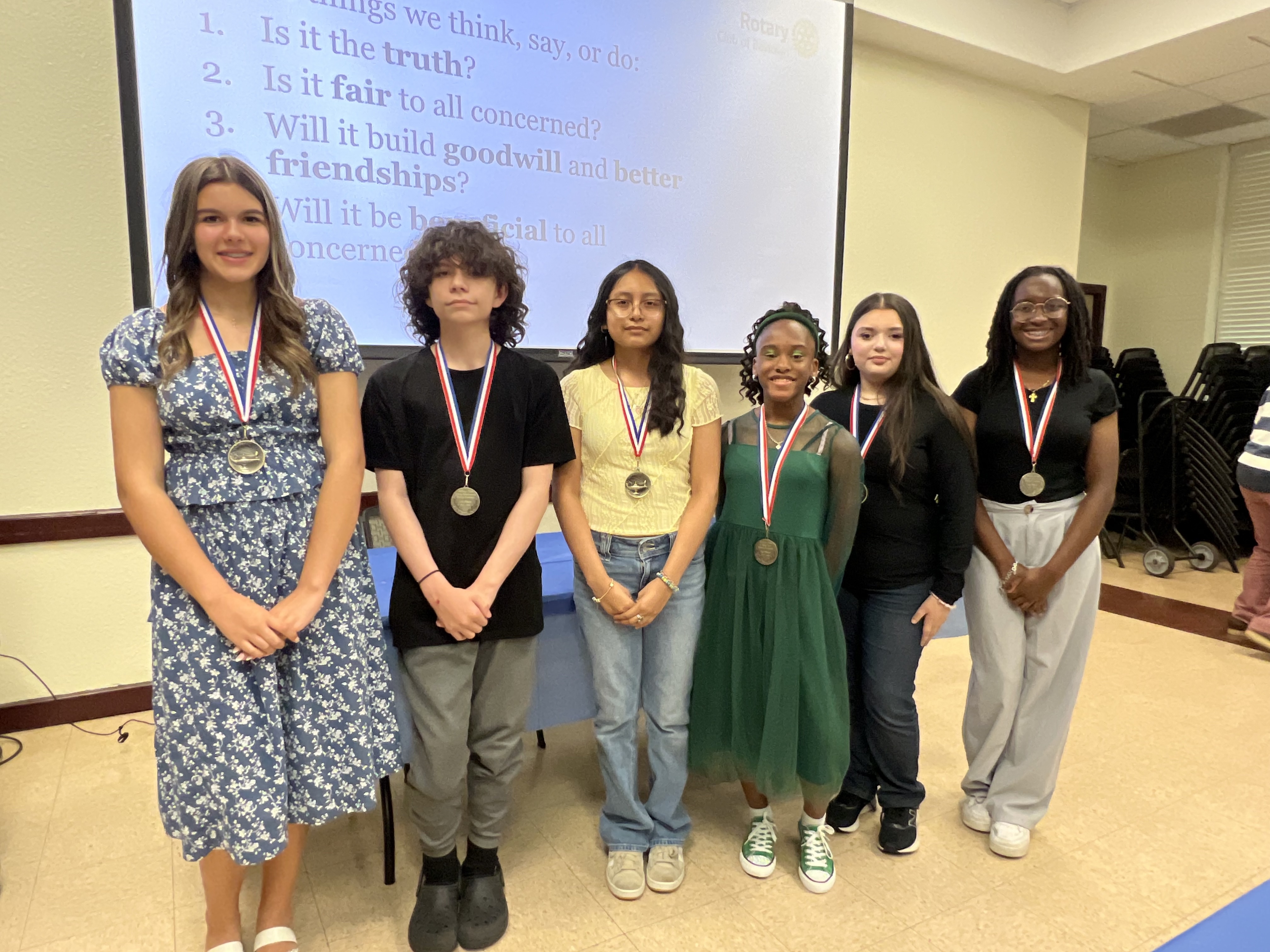 Essay winners pose with awards in classroom with a projector behind them.