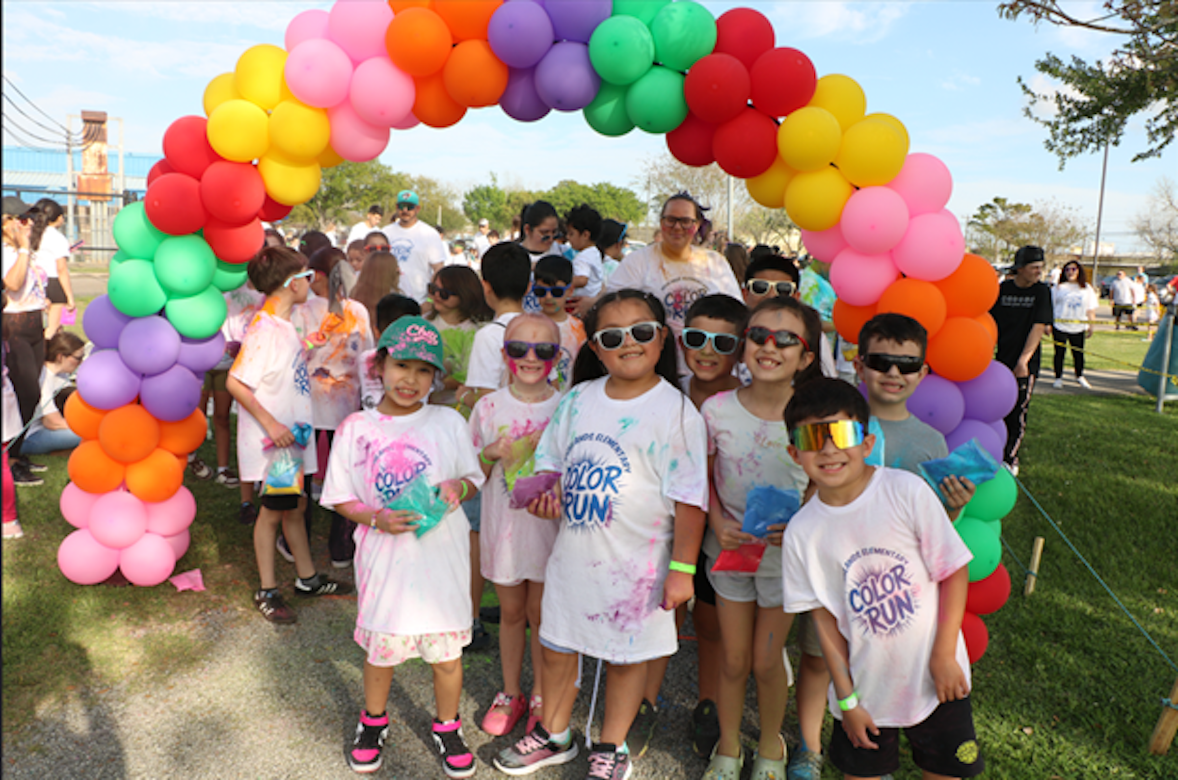 highlands students in white shirts stand in front of rainbow ballooon arch
