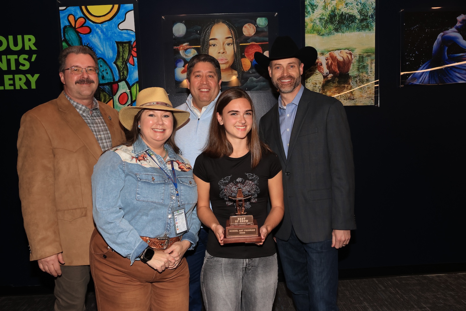 best in show student winner poses with district leaders and teacher while holding her award